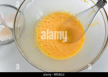 Vista ravvicinata della panna uova nella ciotola di vetro, mescolare con  una frusta elettrica e rotture di vuoto guscio d'uovo su sfondo bianco Foto  stock - Alamy