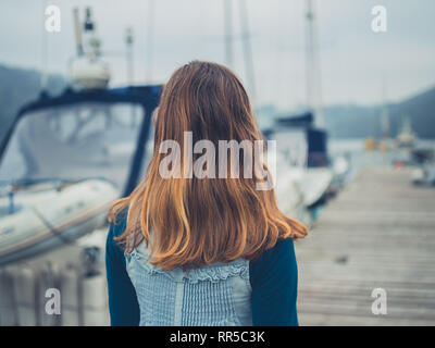 Una giovane donna è camminare in un marina con barche Foto Stock