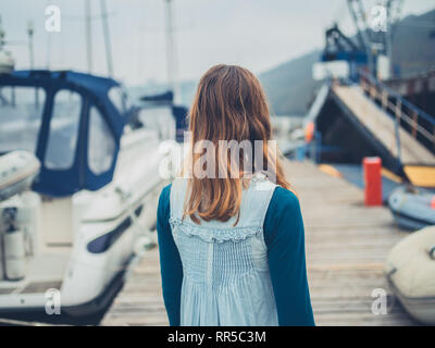 Una giovane donna è camminare in un marina con barche Foto Stock
