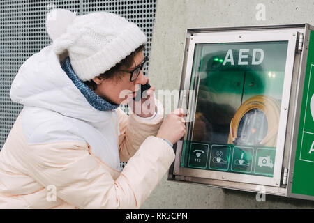 Medicina rianimazione cardiopolmonare chiamata di emergenza. La donna caucasica utilizza telefono chiamando 911 aiuto. il riquadro del dispositivo aed defibrillatore automatico malattia Foto Stock