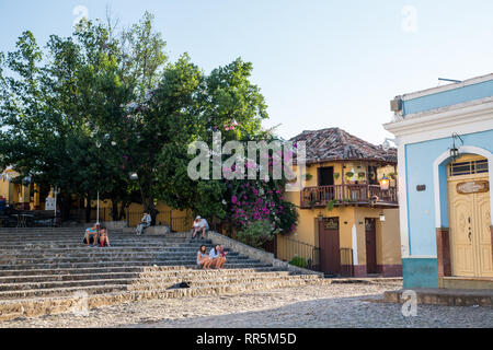 Turisti che si siedono sui gradini vicino a ristoranti locali in una piazza all' incrocio di calle Rosario e Calle Cristo nel centro di Trinidad, Cuba Foto Stock