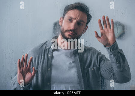 Bello sconvolto l uomo di toccare la finestra con le gocce di pioggia e guardando lontano Foto Stock