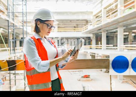 Ritratto di femmina adulta builder, ingegnere, architetto, inspector manager al sito in costruzione. Donna con piano, digitale compressa. Foto Stock