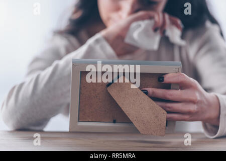 Vista ritagliata di turbare la donna azienda cornice immagine e pianto a casa Foto Stock