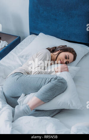 Triste donna in pigiama cuscino di contenimento e giacente nel letto di casa Foto Stock