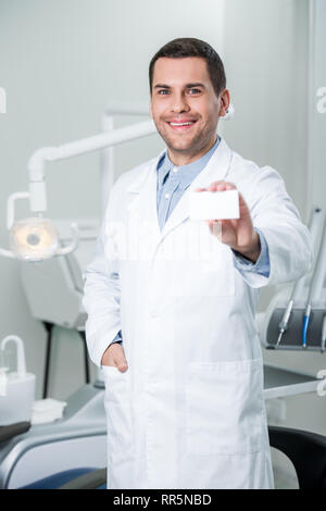 Allegro dentista in piedi con la mano in tasca e tenendo la scheda vuota Foto Stock