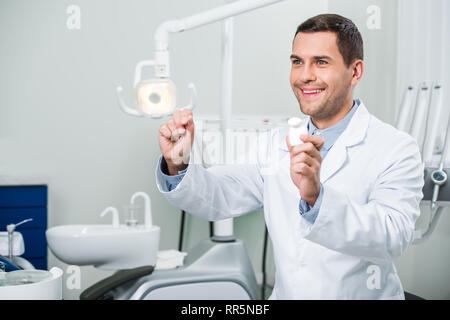 Bello il dentista in camice bianco a sorridere mentre si tiene il filo interdentale Foto Stock