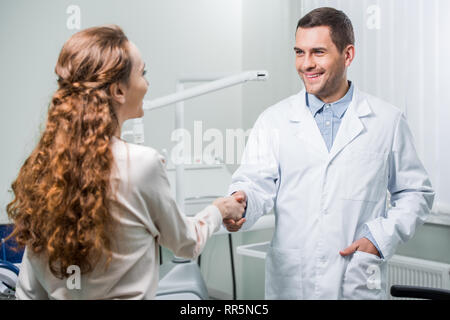 La donna si stringono la mano con il dentista in piedi con la mano in tasca Foto Stock