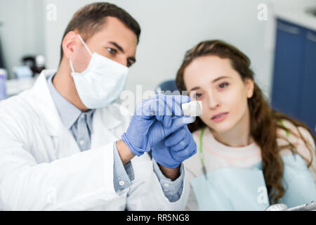 Messa a fuoco selettiva dei raggi x dei denti nelle mani di dentista di guanti in lattice e maschera vicino al paziente Foto Stock