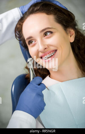 Messa a fuoco selettiva della donna in parentesi graffe sorridere mentre guardando il dentista durante l'esame Foto Stock