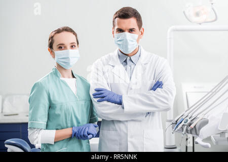 Dentista femmina in maschera in piedi vicino a un collega con bracci incrociati in clinica dentale Foto Stock