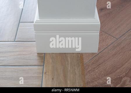 Laminato pavimenti in parquete, piastrelle immitating pavimento di legno duro. Compensatore di sughero come un adattatore. Luce a parete opaco, bianco battiscopa Foto Stock