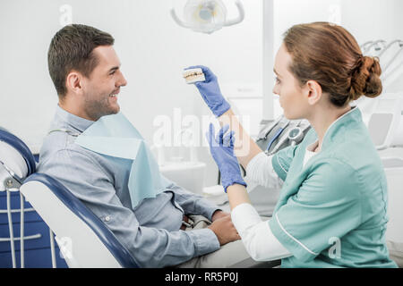 Dentista femmina che mantiene i denti modello vicino al paziente sorridente Foto Stock