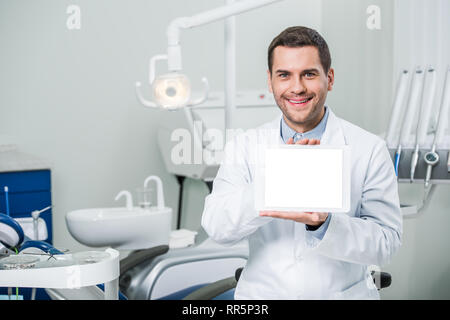 Allegro dentista holding tavoletta digitale con schermo vuoto in clinica dentale Foto Stock