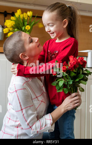 Felice Festa della mamma Festa di compleanno o di sfondo. Adorabile ragazza giovane sorprende la sua mamma, giovane malato di cancro, con bouquet di rose rosse. Festa di famiglia Foto Stock