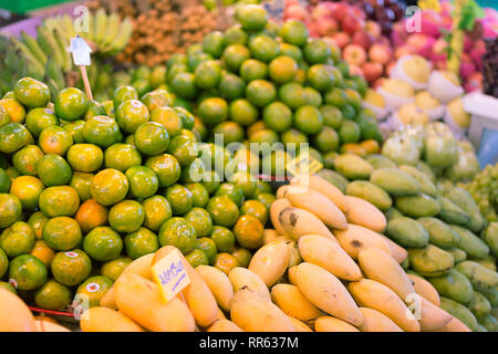 Frutta fresca, arance verde e giallo mango impilati su un mercato in stallo pronto per la vendita. Foto Stock