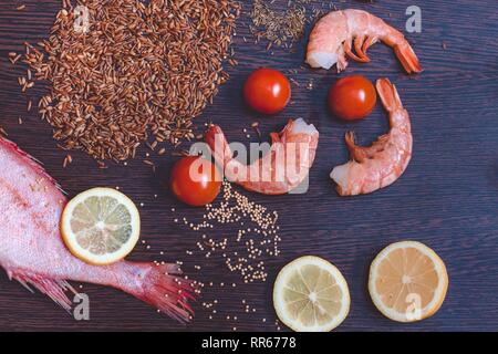 Ingredienti per la cucina indiana sono su un nero superficie di legno. La composizione del piatto include pesce cernia, spicchi di limone, un trito di cipolla, marrone r Foto Stock