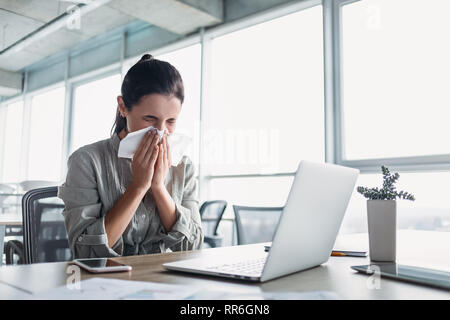 Ill giovani dai capelli scuri catturati donna freddo starnuti in tessuto in ufficio, malati ragazza allergica soffiaggio, tergi esecuzione di naso, avuto influenza, riniti, sinusiti, c Foto Stock