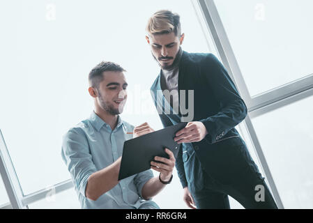 Due imprenditori sorridente parlando di investimenti ammissibili, manager presentando una relazione finanziaria che mostra buoni risultati di lavoro al suo collega, puntando su Foto Stock