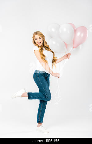 Felice donna bellissima tenuta aria di festa palloncini mentre in piedi su una gamba sola su sfondo bianco Foto Stock