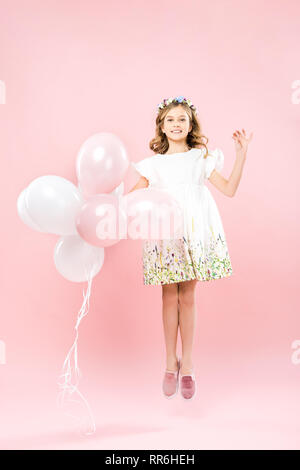 Bambino felice in elegante abito bianco jumping con aria palloncini su sfondo rosa Foto Stock