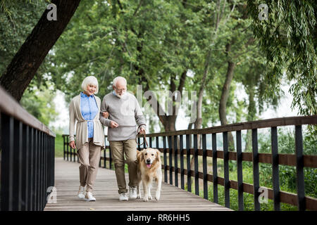 Coppia senior attraversando a piedi il ponte di legno con il cane al guinzaglio Foto Stock