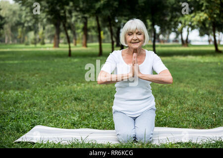 Senior donna sul materassino yoga nella meditazione seduta sukhasana posano con le mani giunte Foto Stock