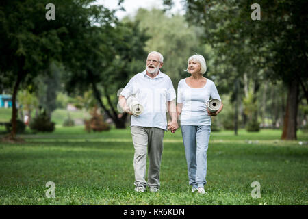 Felice coppia senior passeggiate nel parco e di contenimento materassini fitness Foto Stock