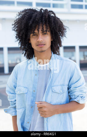 Latin American giovane uomo adulto con lunghi capelli ricci all'aperto in città Foto Stock