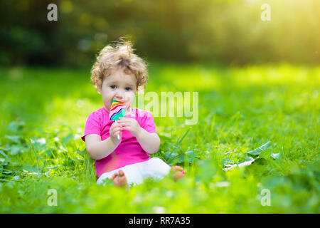 Baby girl a mangiare il gelato candy nel soleggiato parco. Bambino con lollipop. Bambini a giocare all'aperto in estate. Bambino con snack dolce. I bambini mangiano i dolci. Kid Foto Stock