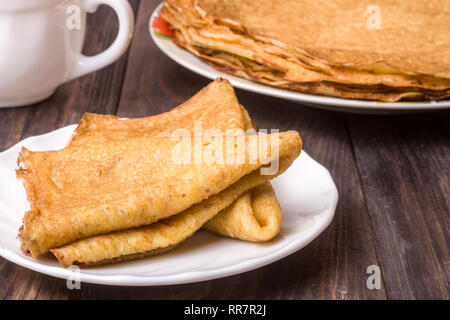 Frittelle di sottile su una piastra bianca con uno sfondo di legno Foto Stock