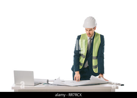 Architetto maschio in casco e giubbotto di sicurezza lavorando con blueprint e laptop, isolato su bianco Foto Stock