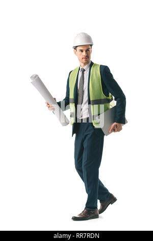 Architetto maschio in casco e giubbotto di sicurezza a piedi con blueprint e laptop, isolato su bianco Foto Stock
