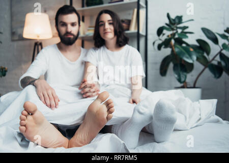 Coppia giovane in pigiama sdraiato sul letto e guardando la fotocamera a casa Foto Stock