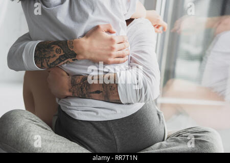 Vista ritagliata della tatuato uomo appassionatamente abbracciando la donna a casa Foto Stock