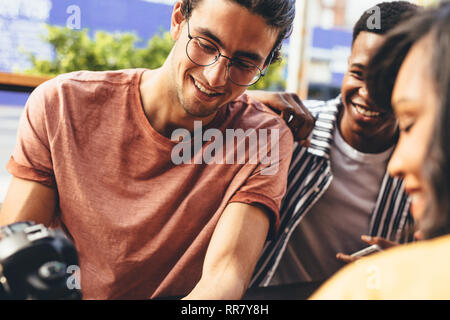 Giovane ragazzo che mostra i suoi contenuti di media sociali sulla fotocamera digitale per gli amici presso il cafe. L'uomo partecipe della sua ultima foto riprese con gli amici. Foto Stock