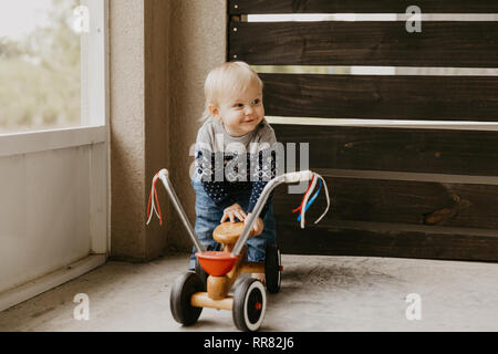 Preziosi carino adorabile piccola bionda Baby Toddler Boy Kid giocando fuori sul giocattolo di legno Noleggio Scooter sorridente Mobile alla fotocamera e divertirsi Foto Stock