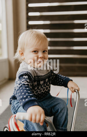 Preziosi carino adorabile piccola bionda Baby Toddler Boy Kid giocando fuori sul giocattolo di legno Noleggio Scooter sorridente Mobile alla fotocamera e divertirsi Foto Stock