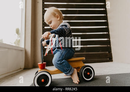 Preziosi carino adorabile piccola bionda Baby Toddler Boy Kid giocando fuori sul giocattolo di legno Noleggio Scooter sorridente Mobile alla fotocamera e divertirsi Foto Stock