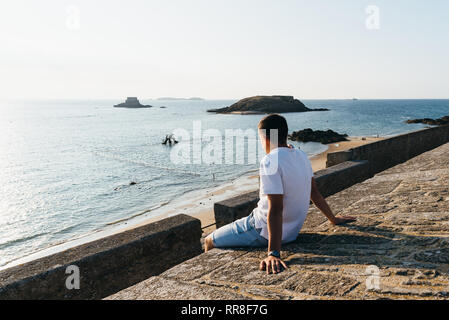 Giovane uomo è guardare il tramonto sulla baia di Saint Malo da bastioni. Vista posteriore con spazio per la copia Foto Stock