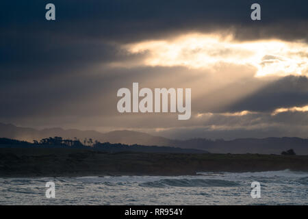 La mattina presto alba con raggi di luce fuori lo streaming di una apertura tra le nuvole, illuminando la costa vicino a Cambria, San Simeone, California. Foto Stock