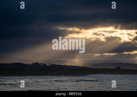 La mattina presto alba con raggi di luce fuori lo streaming di una apertura tra le nuvole, illuminando la costa vicino a Cambria, San Simeone, California. Foto Stock