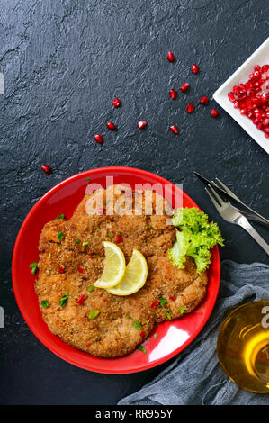 Grande schnitzel viennesi su una targhetta rossa con il limone su uno sfondo nero. Piatto di carne. Vista superiore, piatto laici. Foto Stock