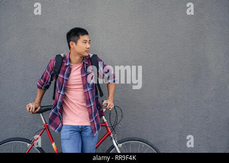 Giovane uomo pendente con la sua moto contro un muro grigio Foto Stock