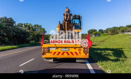 Escavatore terrapieno industriale macchina livellatrice su heavy duty carrello dello scanner a superficie piana è stato trasportato sull autostrada a closeup posteriore campagna fotografica blue sky giorno. Foto Stock