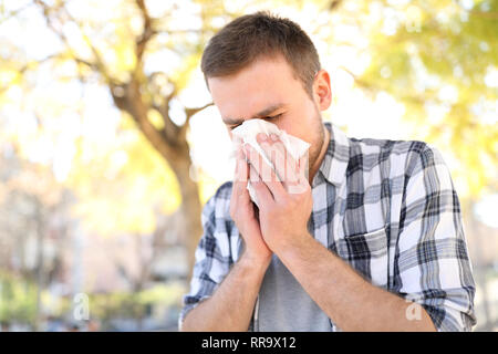 Uomo allergica starnuti che copre il naso con la pulizia in un parco nella stagione primaverile Foto Stock