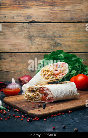 Döner Kebab (shawarma o döner wrap). Pollo alla griglia su lavash (pane pita) con verdure fresche - pomodori, insalata verde, peperoni. Vecchio backgr in legno Foto Stock