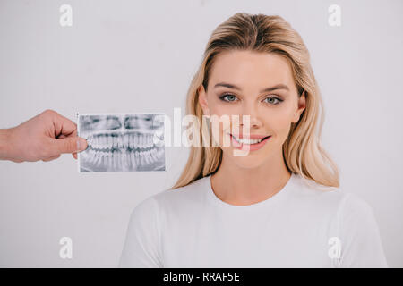 Mano maschio che mantiene i denti x-ray mentre bella donna sorridente in t-shirt guardando la telecamera isolato su bianco Foto Stock