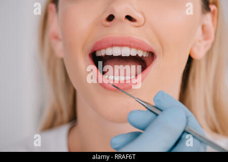 Vista ritagliata di dentista esaminando denti della giovane donna con sonda dentale Foto Stock