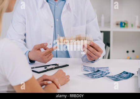 Vista ritagliata di dentista in camice bianco puntando con il dito sui denti tavolozza di colori in clinica Foto Stock